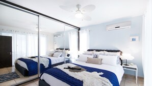 Une chambre moderne avec un grand miroir, deux lits, un ventilateur de plafond et une table de chevet avec une lampe.
