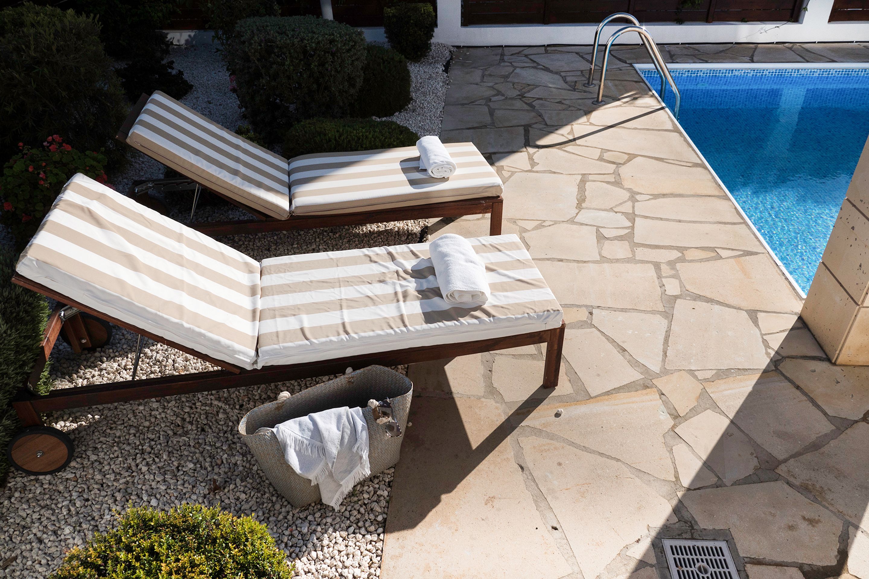 A poolside area with two lounge chairs, a small trash bin, and a stone-tiled deck.
