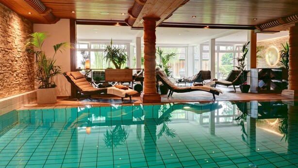 Una piscina interior con paredes y techo azulejados, rodeada de sillones de descanso y plantas en macetas.