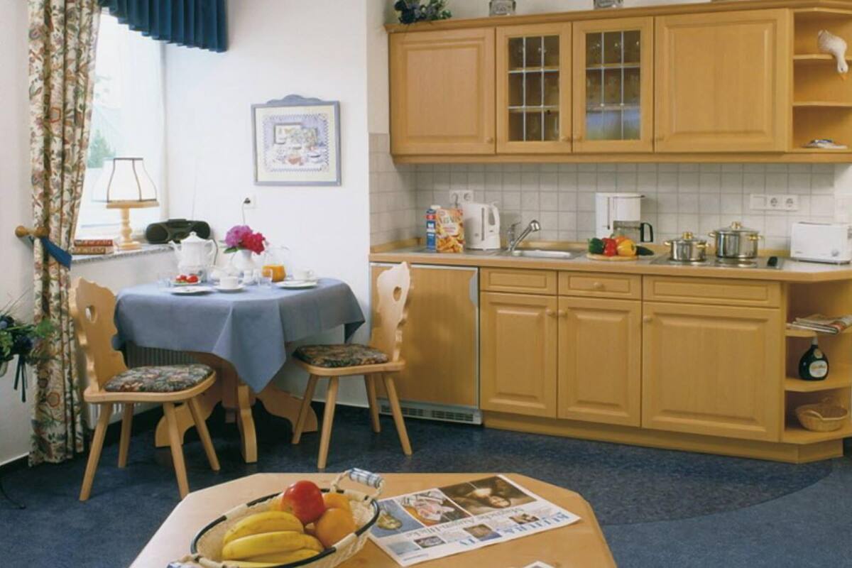 A compact kitchen with wooden cabinets, a dining table with chairs, and a window with curtains.