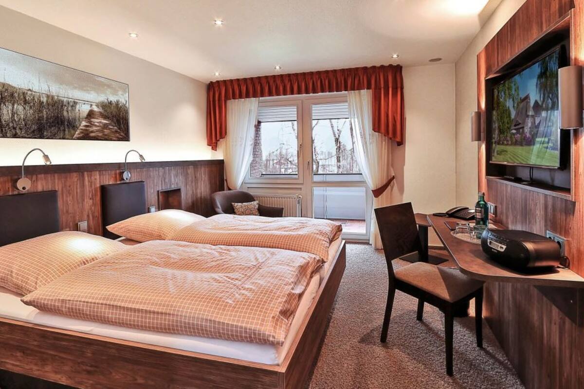 A hotel room with two beds, a desk with a computer, a TV, and a window with curtains.
