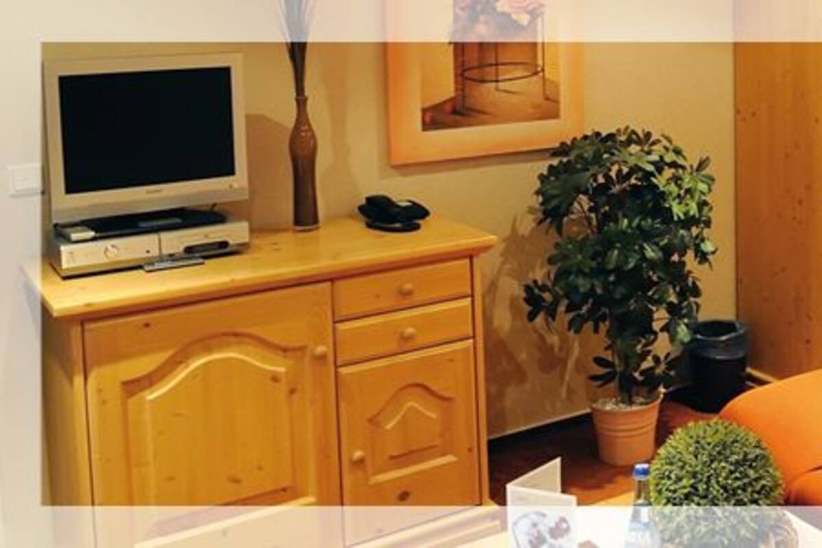 A room with a bed, a desk with a computer, a plant, and a window with curtains.