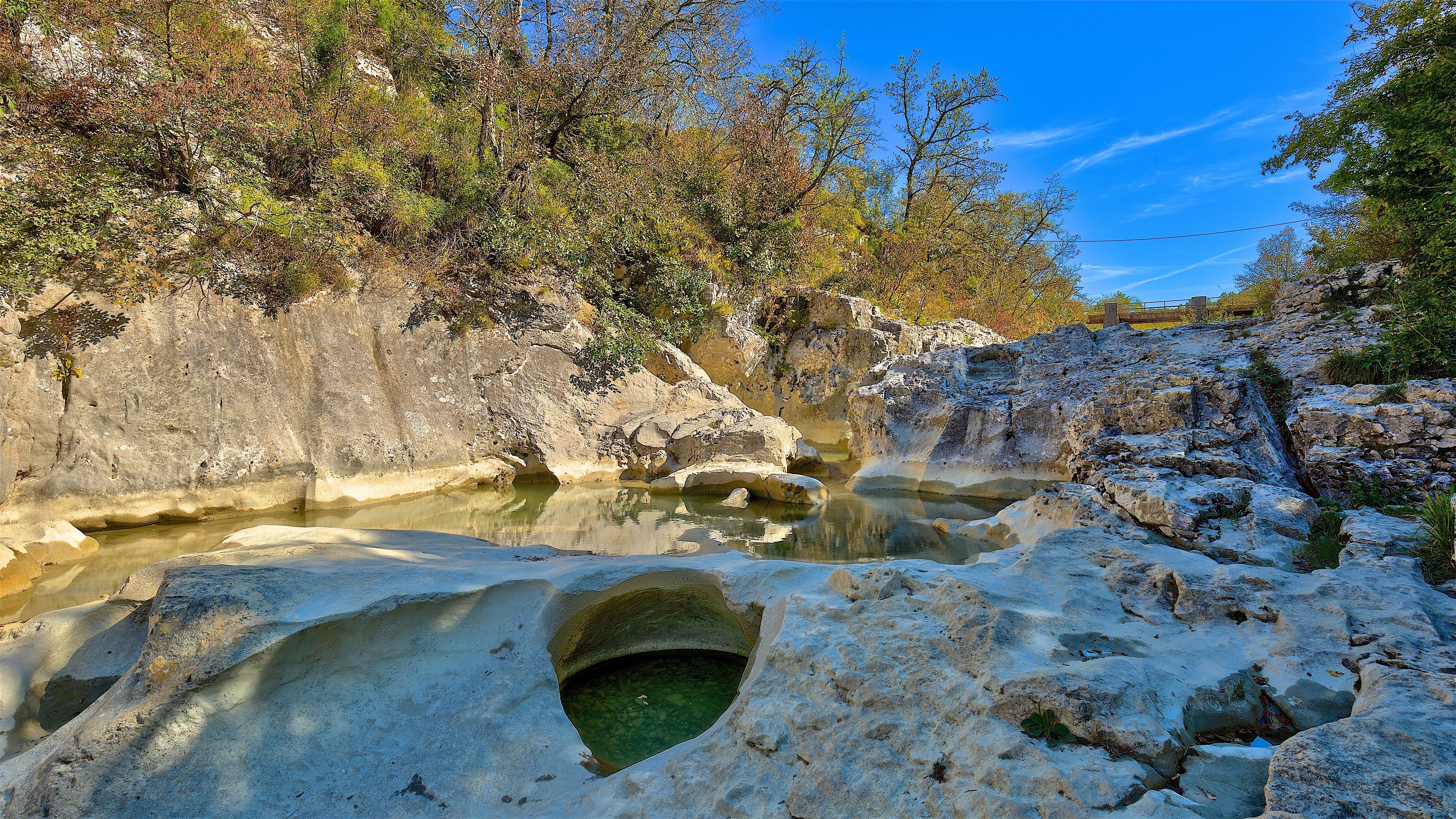 A natural landscape with a rocky terrain, a small stream, and dense foliage.