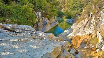 A natural landscape with a rocky terrain and a clear water body surrounded by dense greenery.