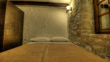 A bedroom with a bed, wooden wardrobe, stone wall, and a window.