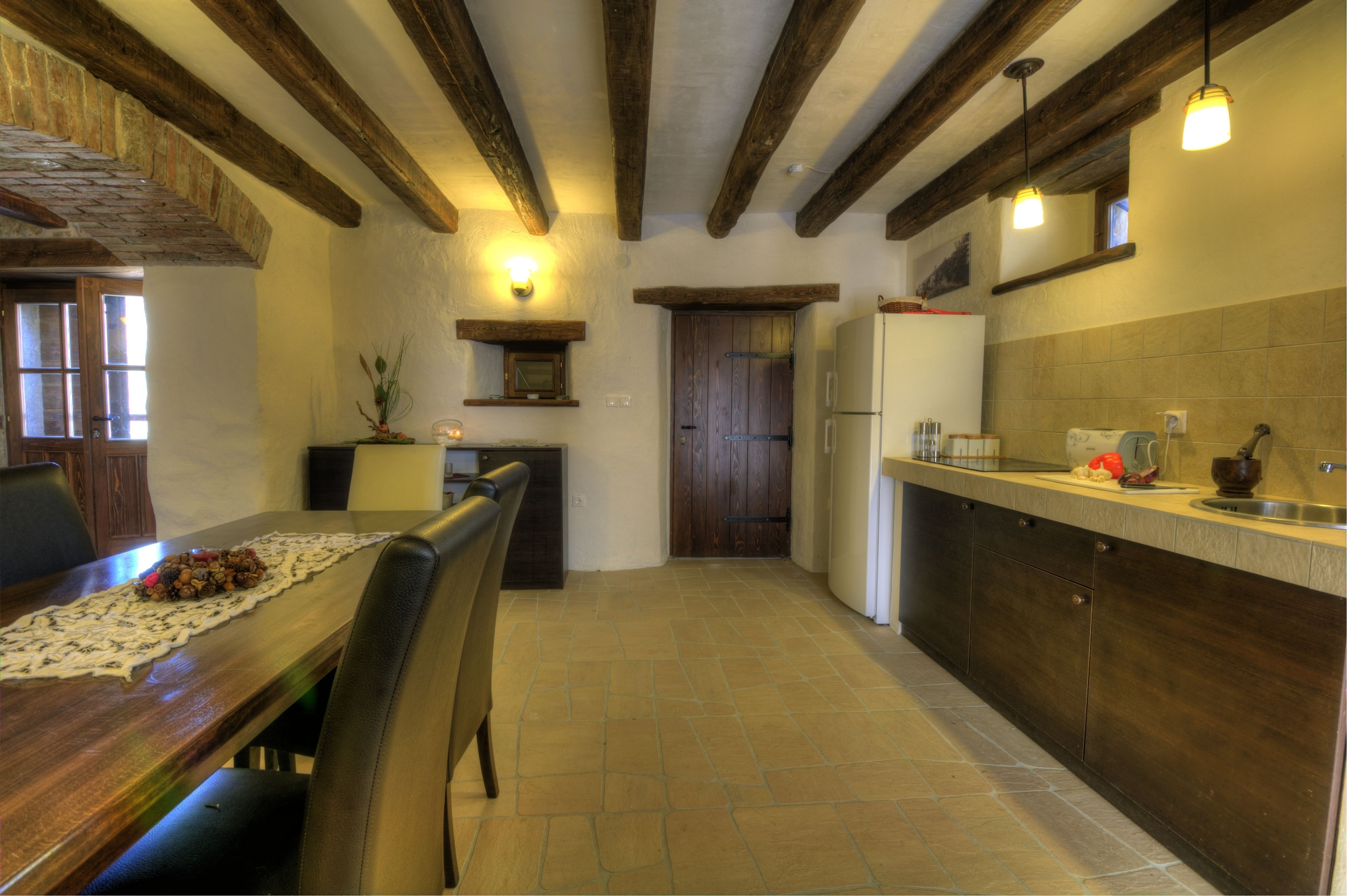 Una cocina con vigas de madera, una mesa de comedor con sillas, un refrigerador y un lavamanos.