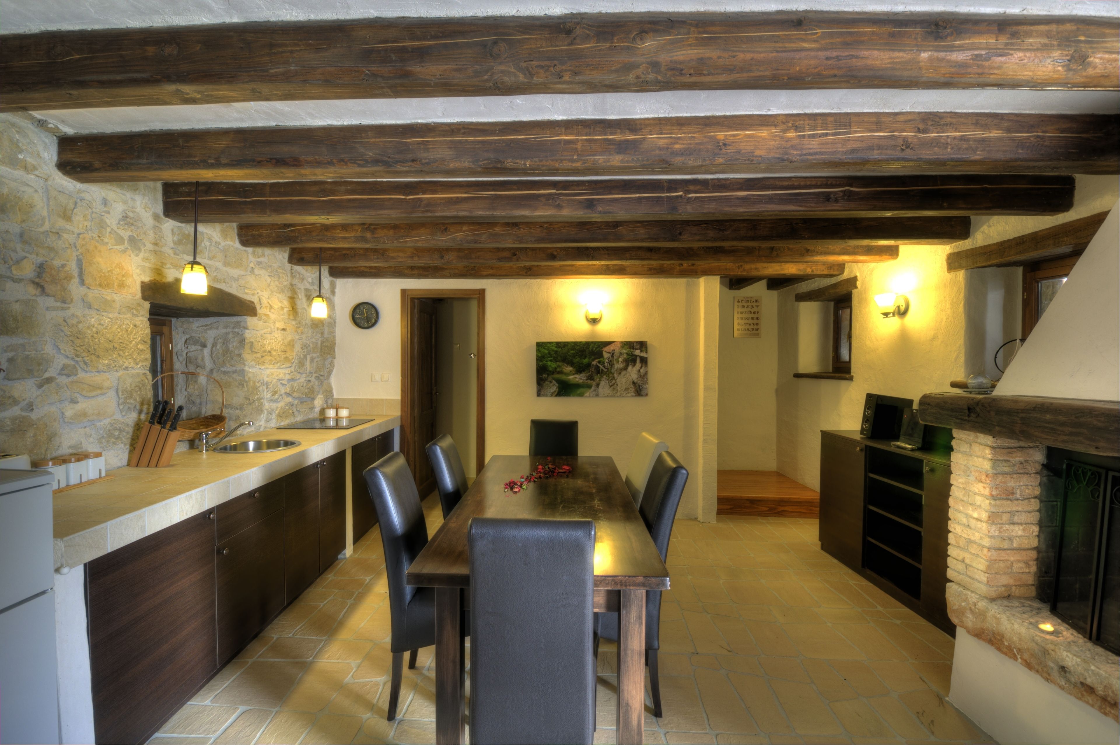 Una cocina rústica con pared de piedra, vigas de madera, una mesa de comedor con sillas y una chimenea.