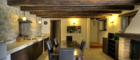 Una cocina rústica con pared de piedra, vigas de madera, una mesa de comedor con sillas y una chimenea.