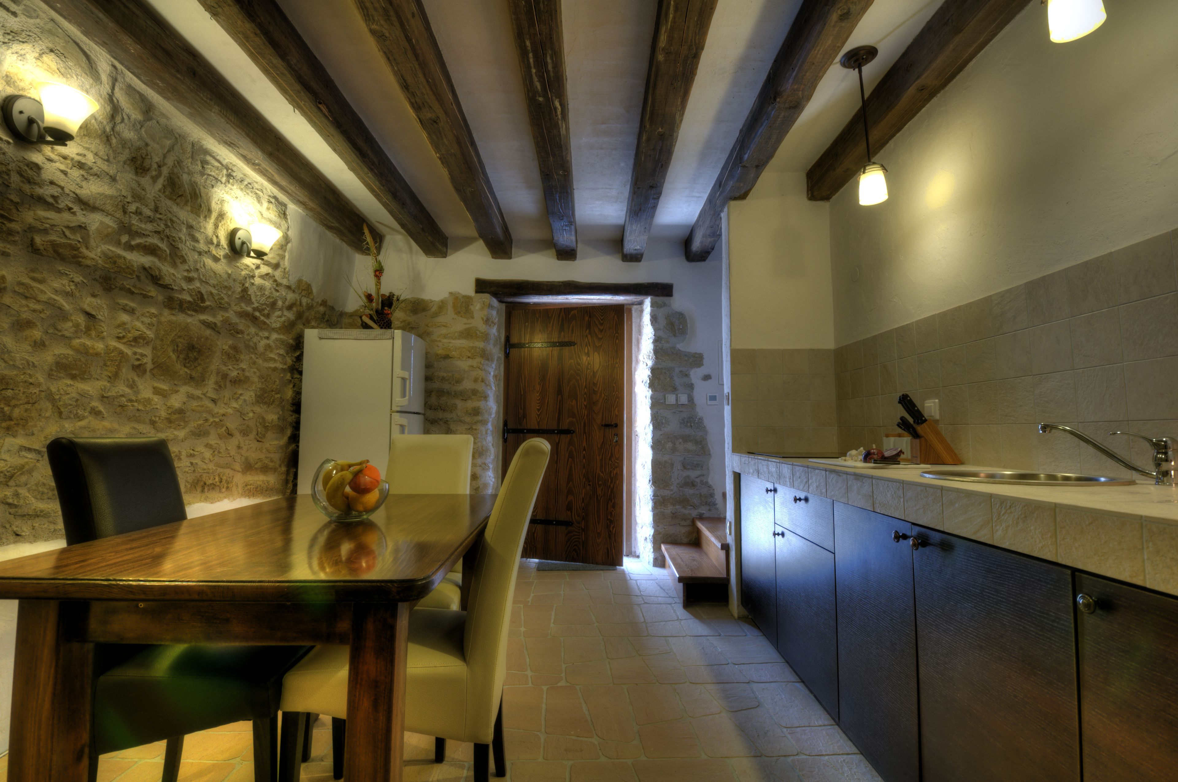 A kitchen with stone walls, wooden beams, a dining table with chairs, and a sink.
