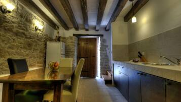 A kitchen with stone walls, wooden beams, a dining table with chairs, and a sink.