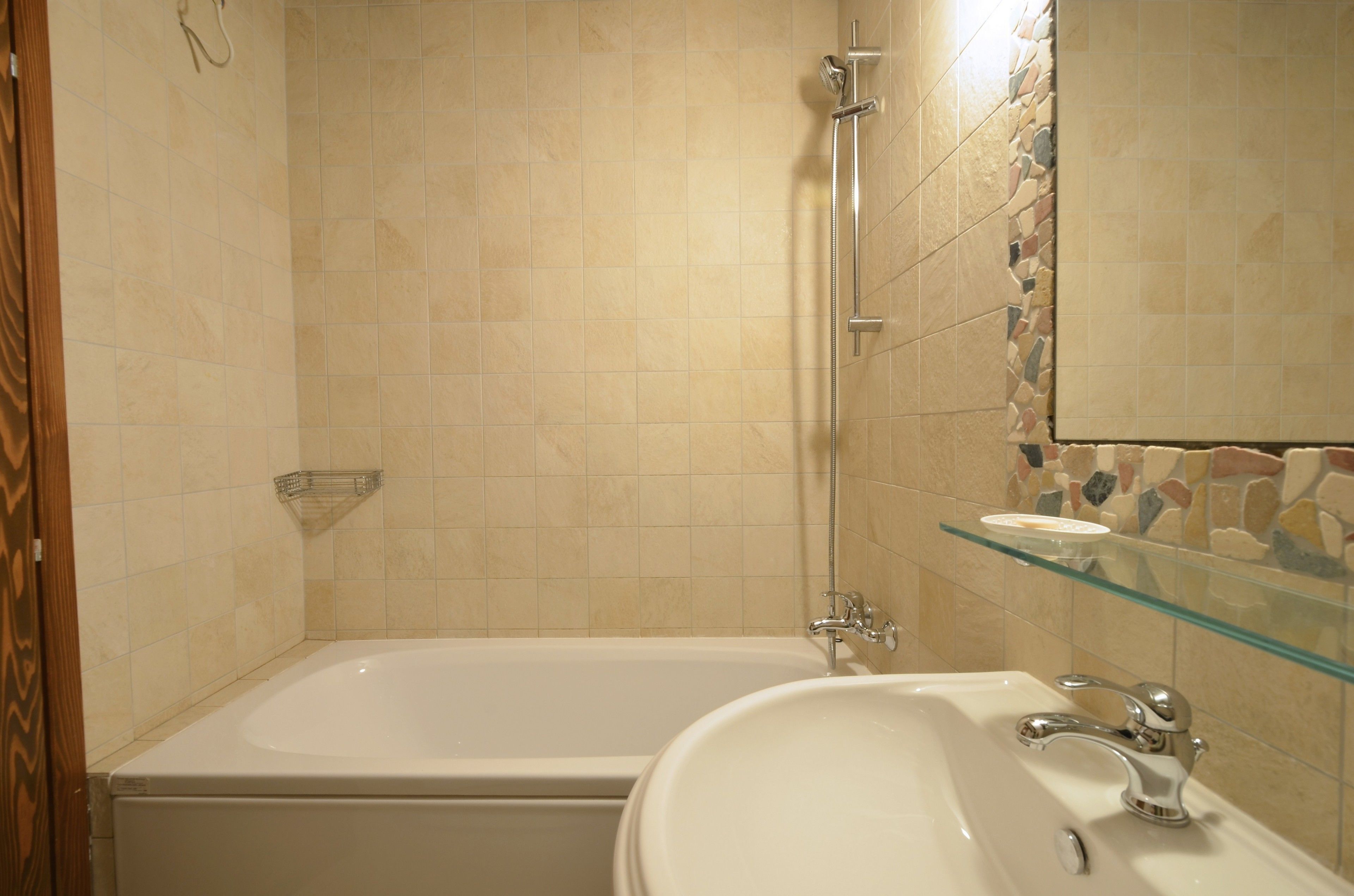 A bathroom with a bathtub, a glass shelf, and a sink.