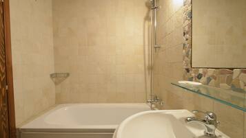 A bathroom with a bathtub, a glass shelf, and a sink.