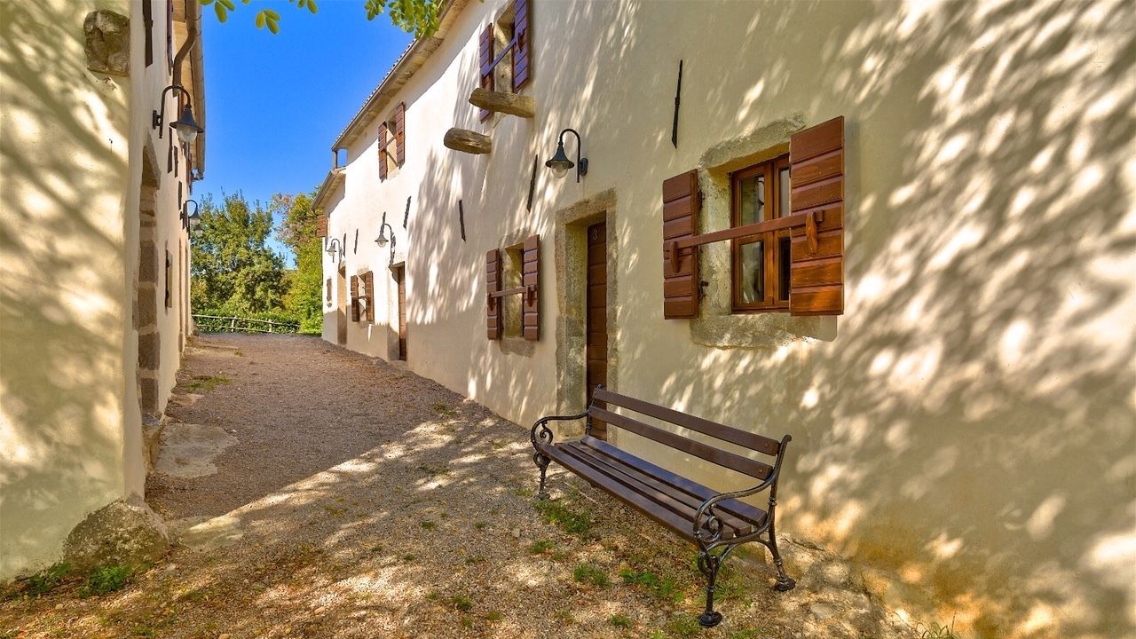 A narrow cobblestone path leading to a white building with wooden shutters and a bench.