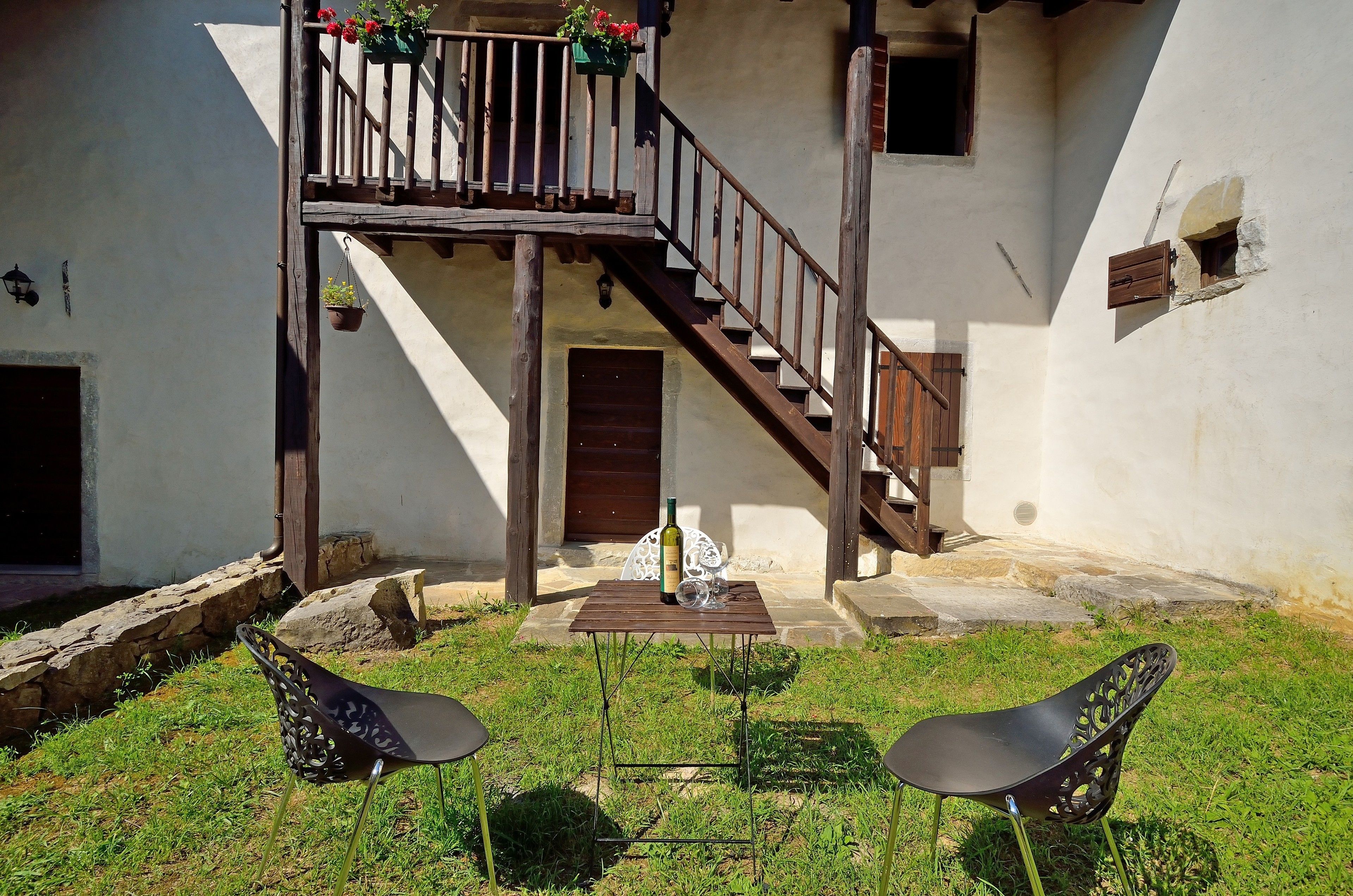 Un patio con una escalera de madera, una mesa con una botella y dos sillas.