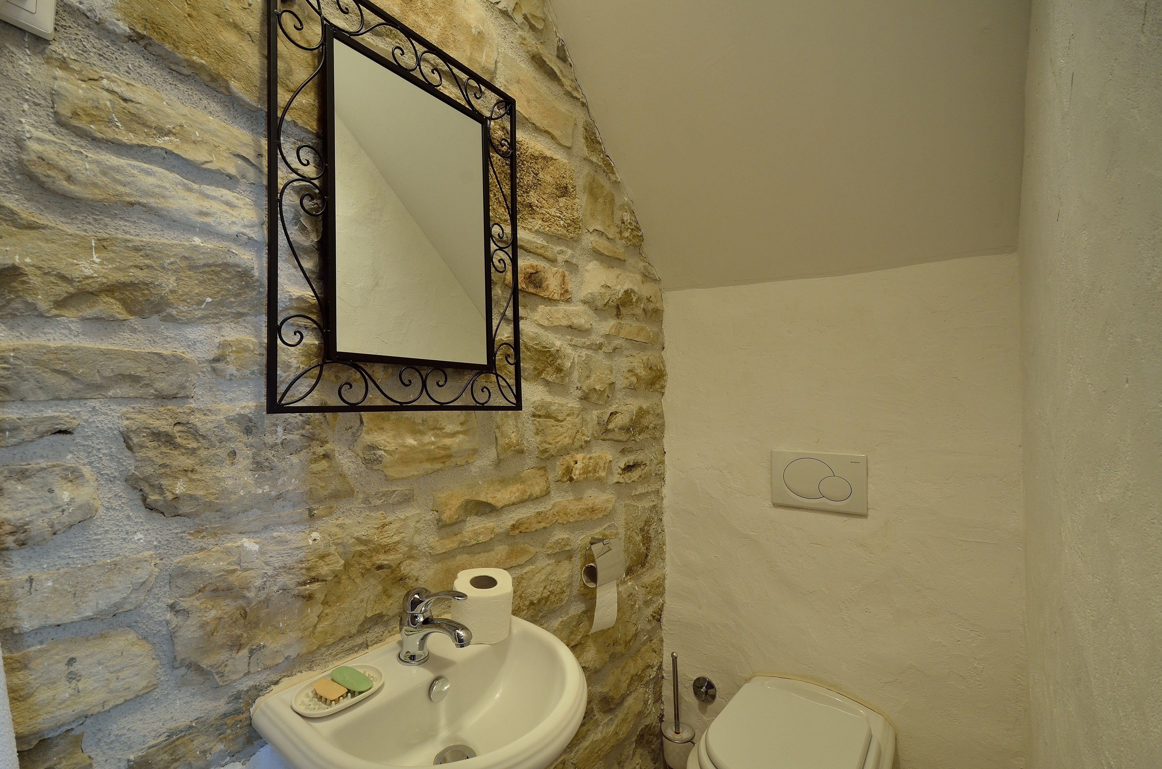 A bathroom with a stone wall, a white sink, a mirror, and a toilet.
