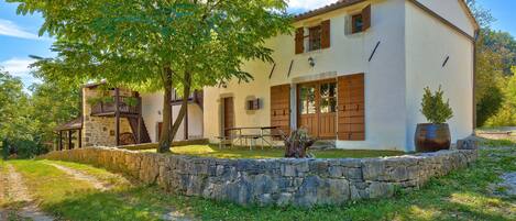 A two-story house with a stone wall, wooden shutters, and a stone staircase.
