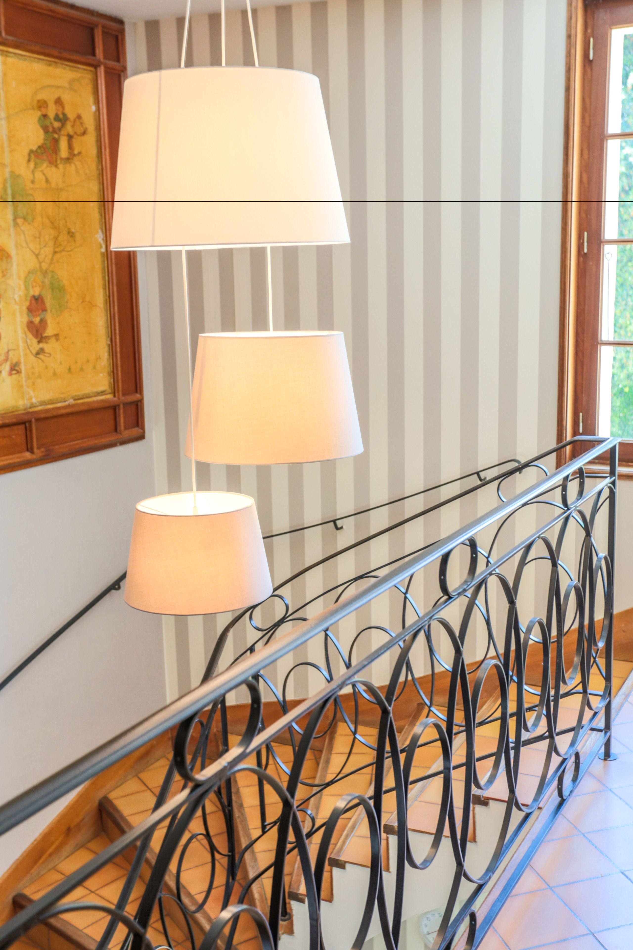 Un escalier avec une rampe en métal et trois lampes suspendues.