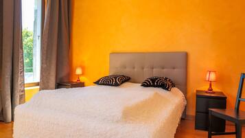 A bedroom with a large bed, two patterned pillows, a nightstand with a lamp, and a chair.