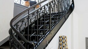A staircase with ornate black metal railings and a geometric-patterned chair in the foreground. - Résidence du Chateau de Bégué (Cazaubon)