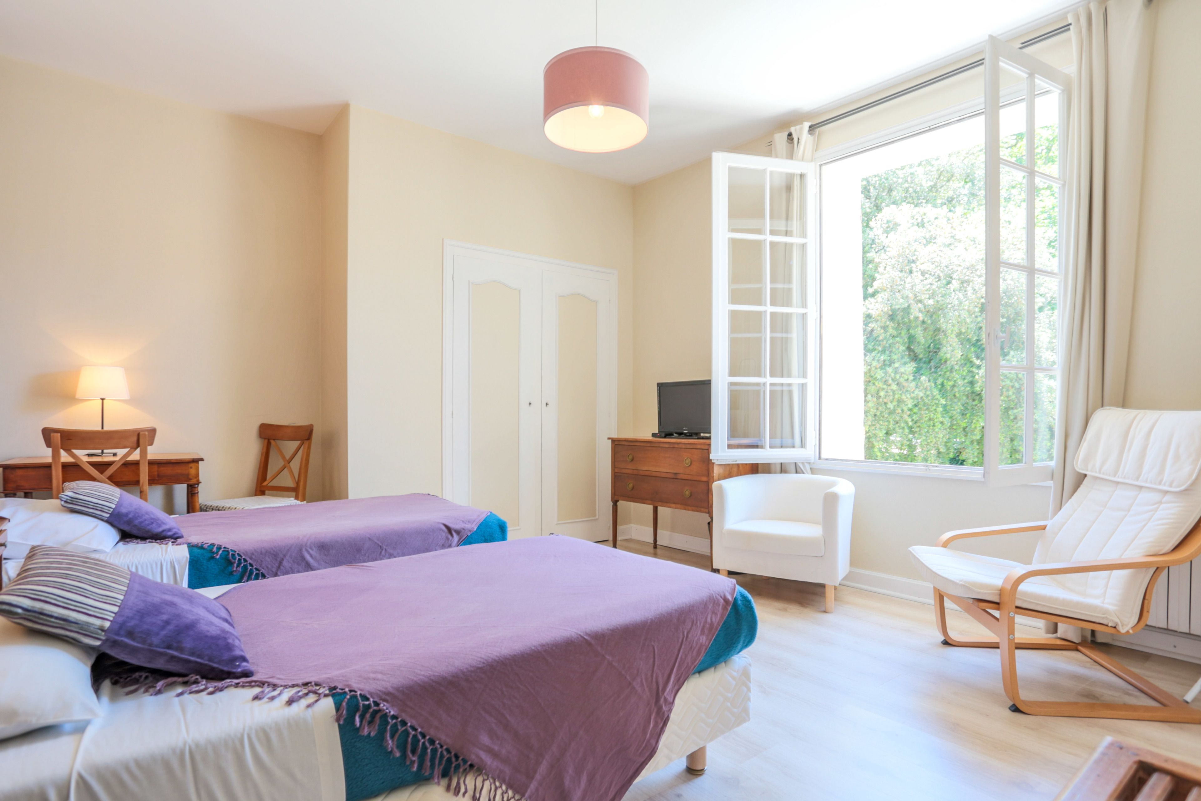 Un dormitorio con dos camas, un escritorio, una silla y una ventana con vistas a zonas verdes.