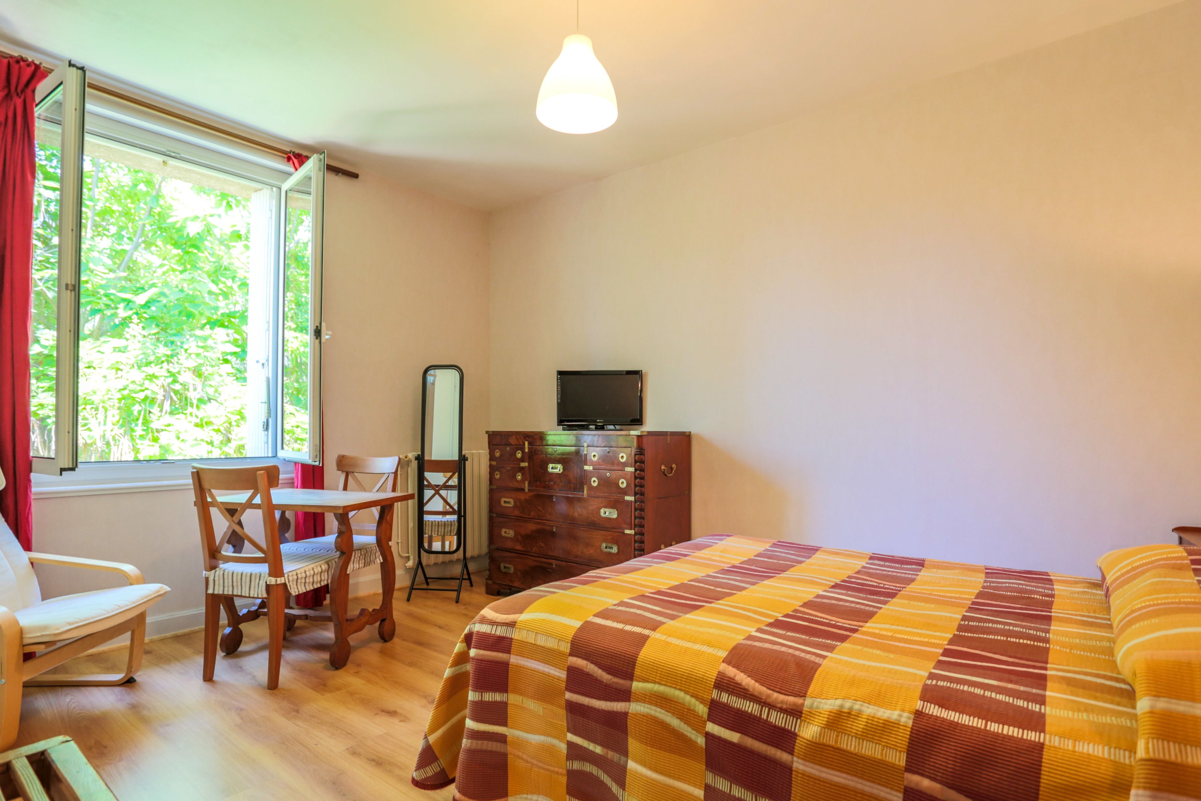 Ein Schlafzimmer mit Bett, Schminktisch, Stuhl, Tisch und einem Fenster mit Vorhängen.