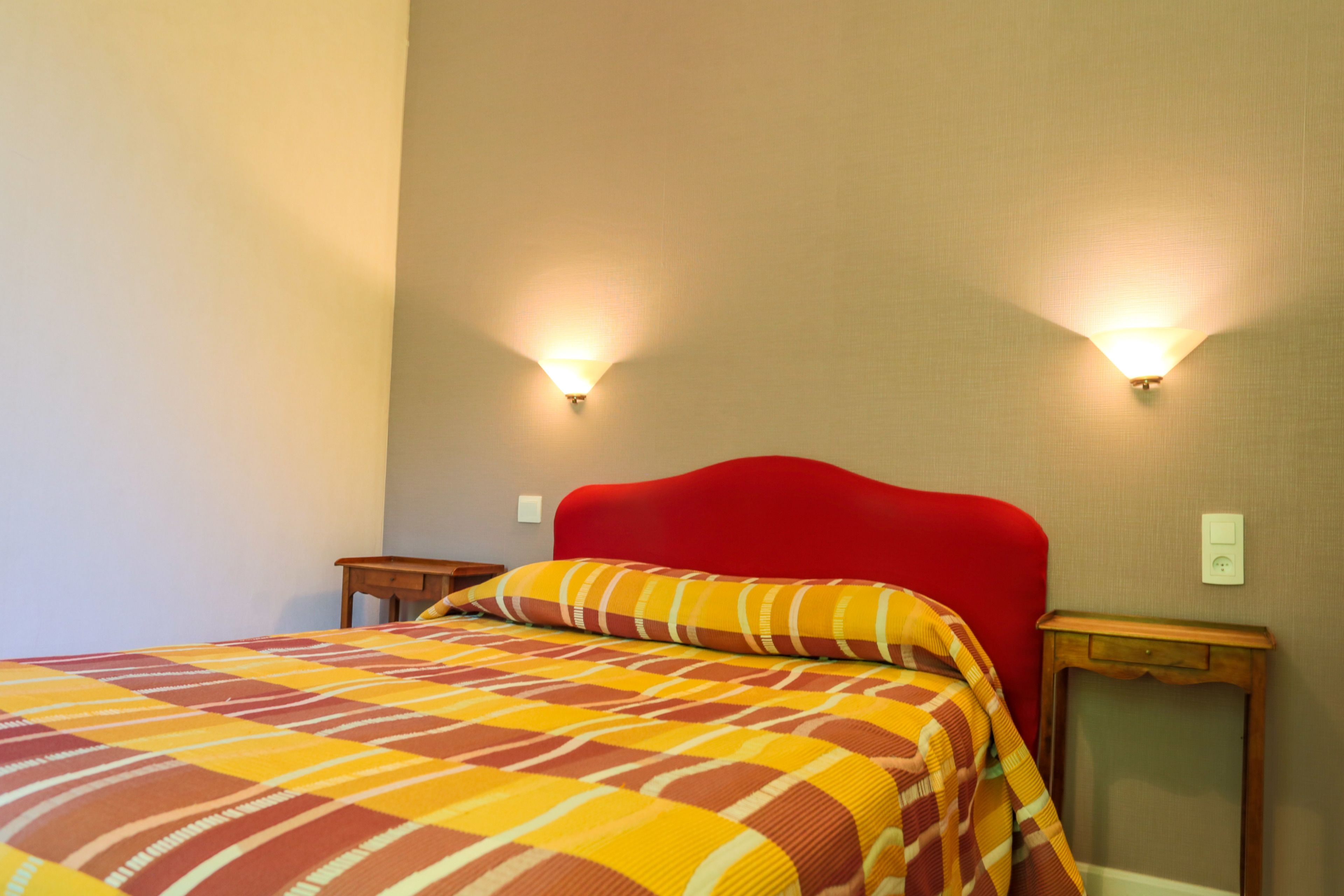 A hotel room with a red headboard, a checkered bedspread, two bedside lamps, and a nightstand.