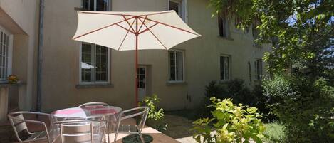 An outdoor patio with a table and chairs, an umbrella, and a building in the background.