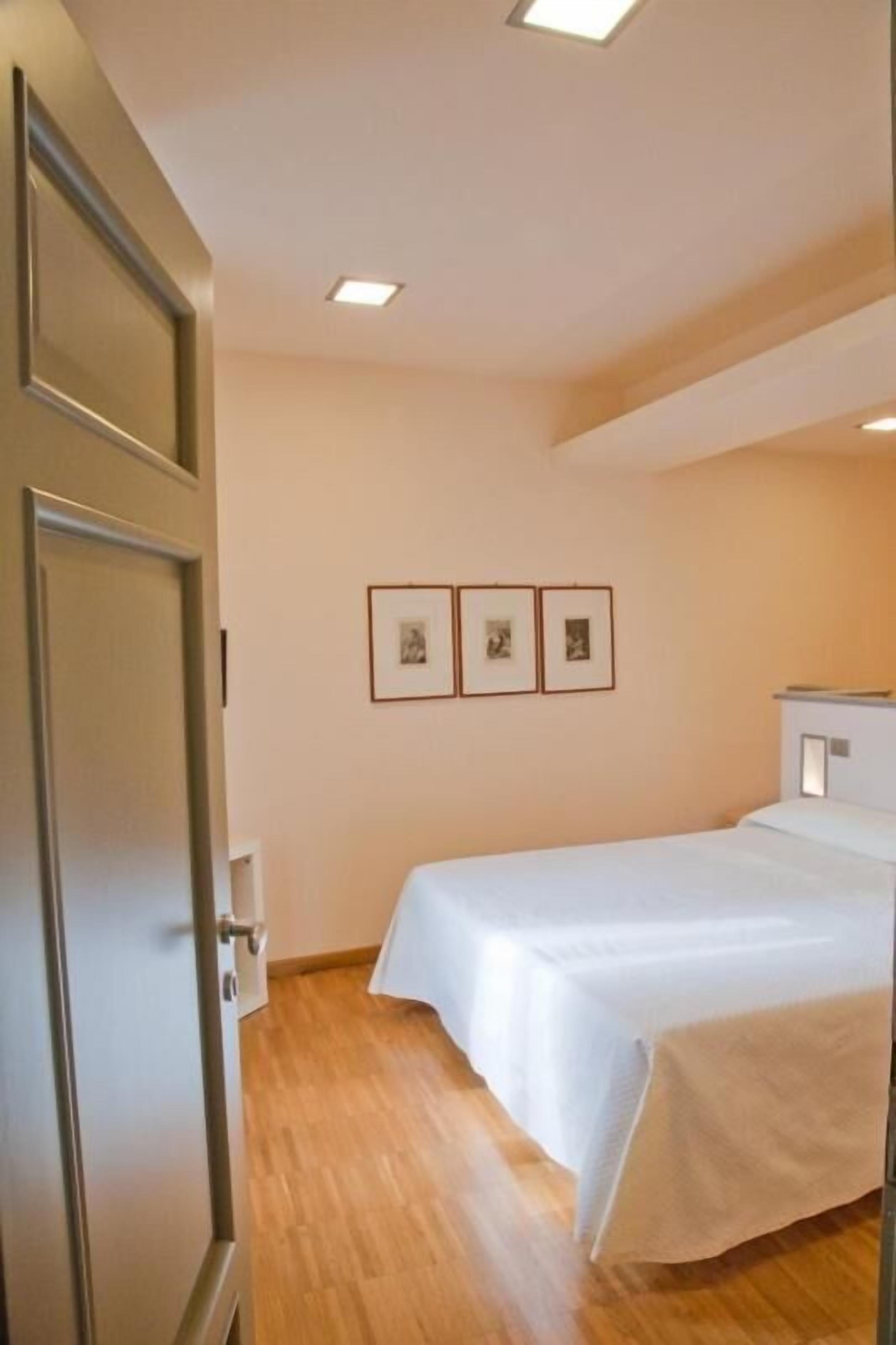 Una camera da letto con pavimento in legno, un letto con biancheria bianca, una porta e tre quadri appesi al muro.