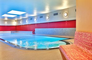 A swimming pool with a red and grey wall, a red lifebuoy, and a tiled bench.