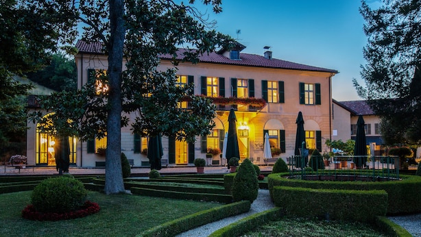 Ein großes, zweistöckiges Gebäude mit einer symmetrischen Fassade, zahlreichen Fenstern und einem gepflegten Garten mit Hecken und Wegen.