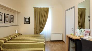 Ein Hotelzimmer mit einem Bett, einem Schreibtisch mit Spiegel, einem kleinen Kühlschrank und einem Fenster mit Vorhängen.