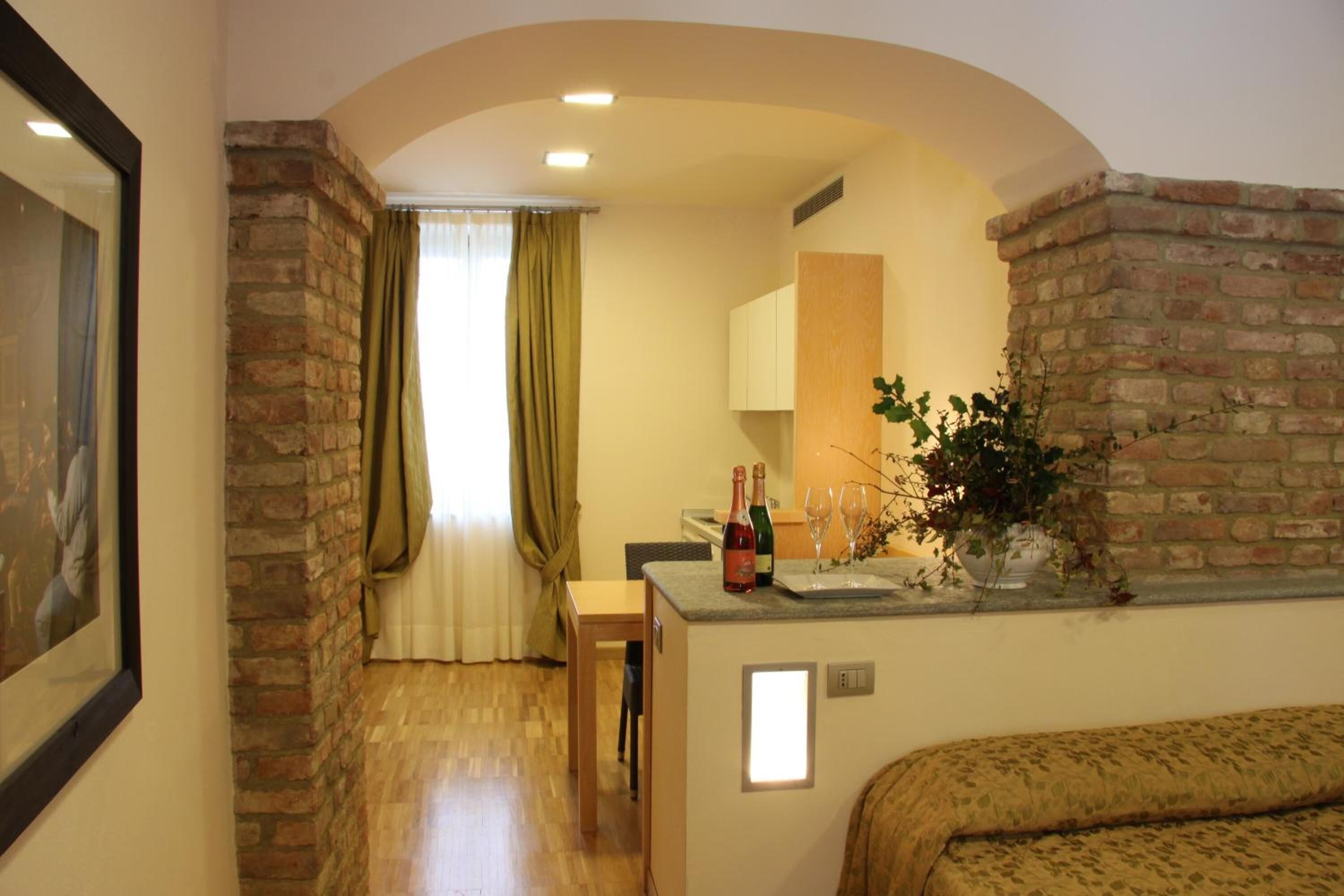 A cozy room with a wooden floor, a sofa, a small table with a bottle and glasses, and a brick wall.