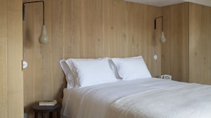 A bedroom with a wooden wall, a bed with white bedding, and two wall-mounted light fixtures. - Quinta da Côrte (Tabuaço)