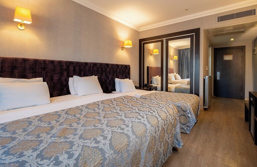 A hotel room with a large bed, two bedside tables, a mirror, and a door leading to a bathroom.