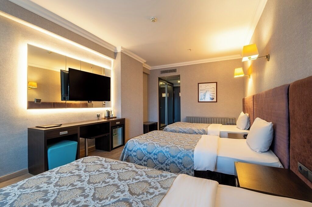 Una habitación de hotel con dos camas, un escritorio con computadora, televisión y baño.