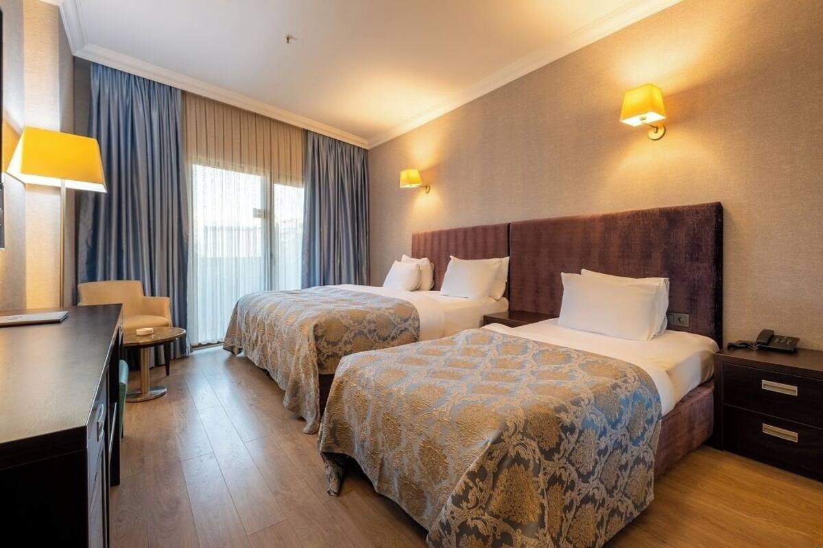A hotel room with two beds, a desk, a chair, a lamp, and a nightstand.