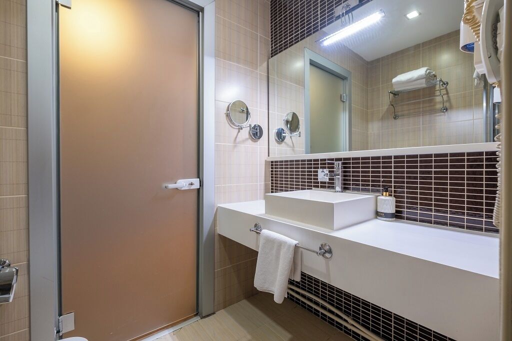 A modern bathroom with a white sink, two round mirrors, a towel rack, and a shower area.