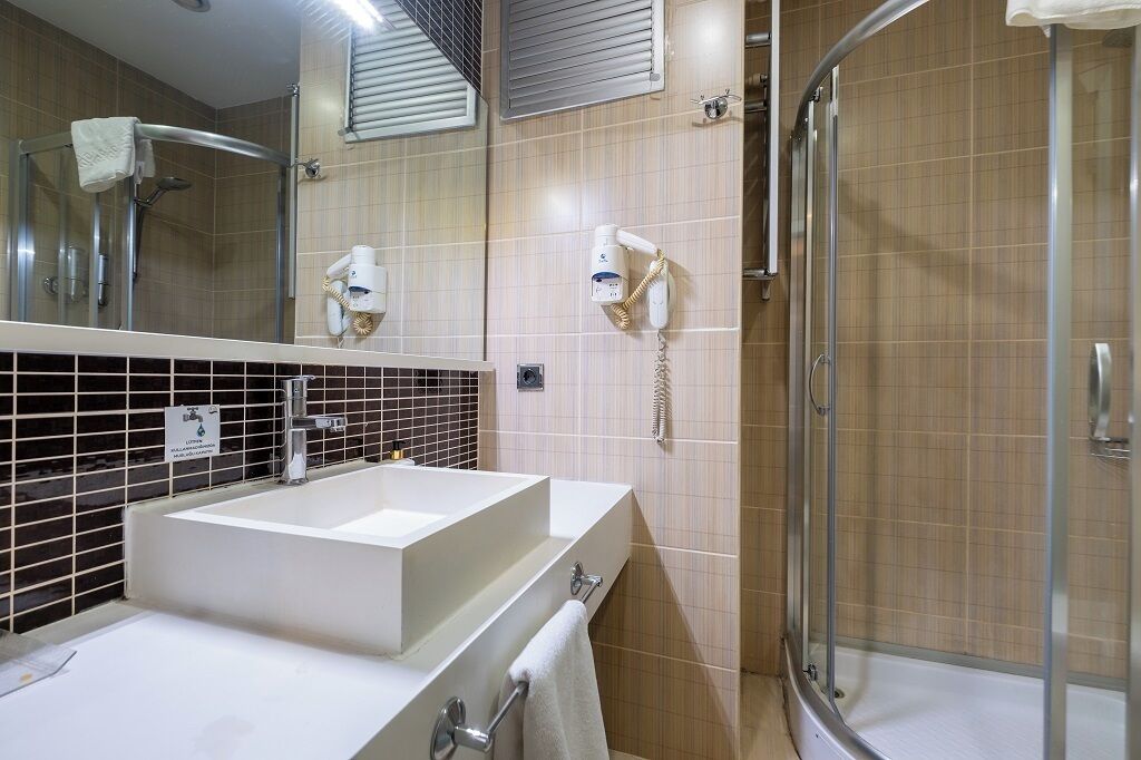 Une salle de bain équipée d’un lavabo, d’un miroir, d’un porte-serviettes, d’une douche et d’un téléphone.