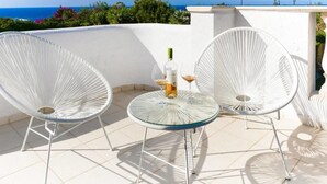 A terrace with two white wicker chairs and a round glass table, a bottle of wine, and two wine glasses. - Villa Siesta (Pegeia)