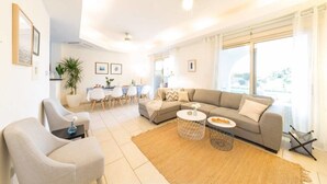 A modern living room with a grey sofa, a round coffee table, and a dining area with a white table and chairs. - Villa Siesta (Pegeia)