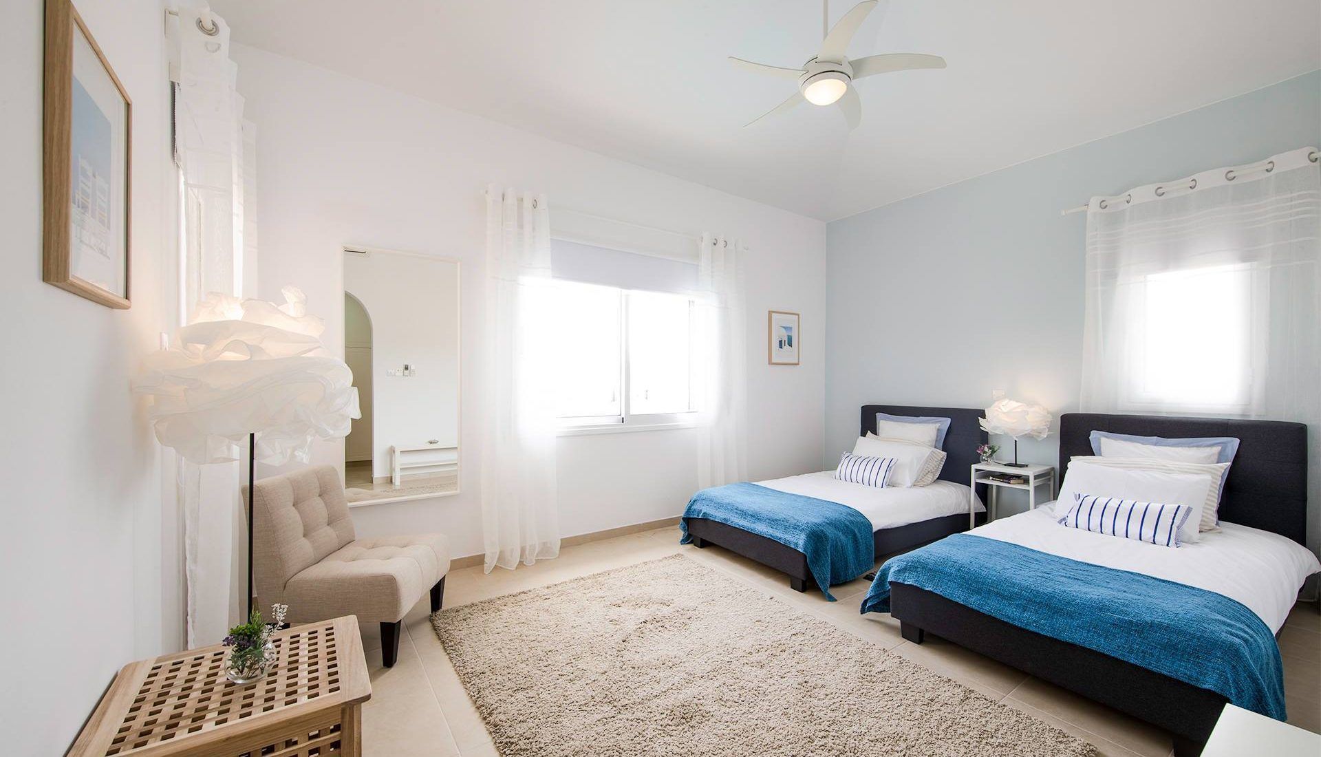 Habitación de hotel con dos camas, una zona de estar con una silla, una mesita y un ventilador de techo.
