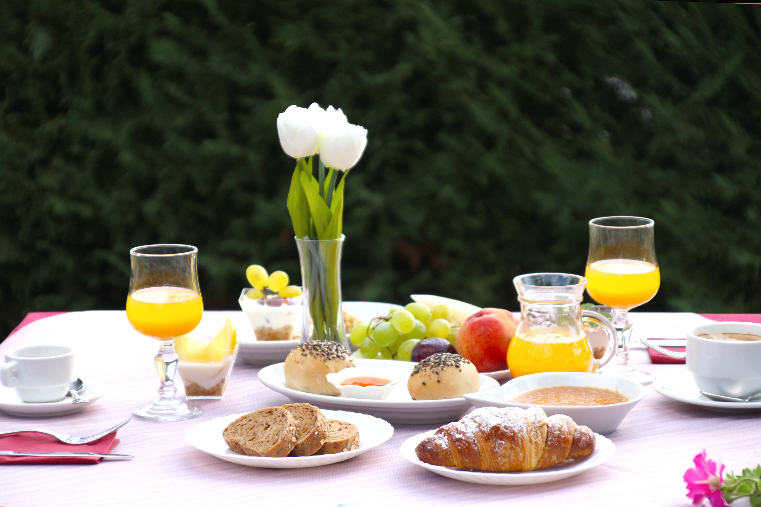 Una mesa de desayuno con platos de comida, vasos de jugo de naranja y un jarrón con flores.