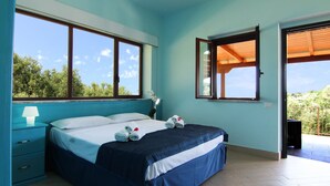 Un dormitorio con cama, mesita de noche, lámpara y vistas al exterior a través de amplias ventanas.