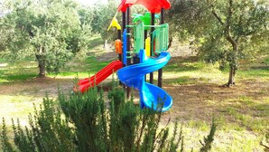 Un parque infantil con un tobogán rojo y azul, rodeado de follaje y árboles.
