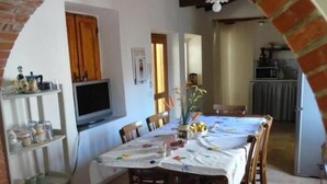A dining area with a brick archway, a TV, and a kitchen in the background. - B&B Domu Incanto (Muravera)