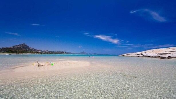 A beach with clear shallow waters, a sandy shore, and rocky formations in the background. - B&B Domu Incanto (Muravera)