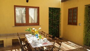 A dining area with a table set for four, surrounded by wooden chairs, with a window and a green wall with climbing plants. - B&B Domu Incanto (Muravera)