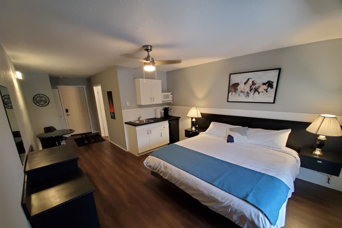 A hotel room with a bed, bedside tables, a desk, a kitchenette, and a bathroom.