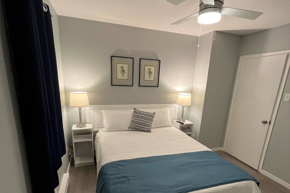 A hotel room with a bed, two bedside lamps, a ceiling fan, and two framed pictures on the wall.