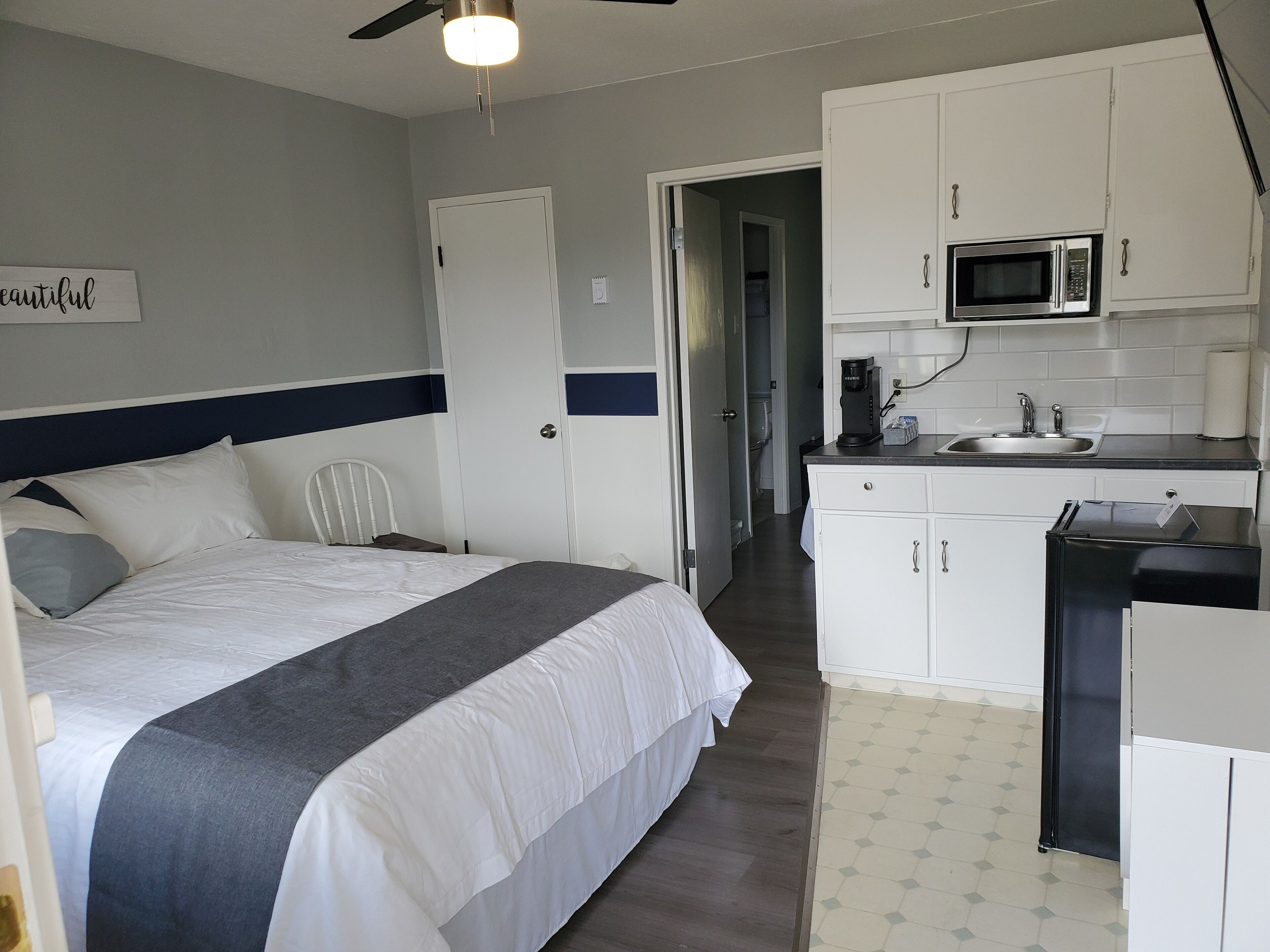 A hotel room with a bed, a kitchenette, and a bathroom visible through an open door.
